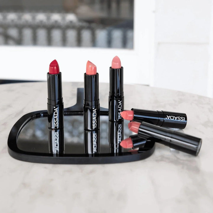 ISSADA Luxury Matte Lipstick collection in bold red, peach, and nude shades displayed on a mirror with sleek black packaging.