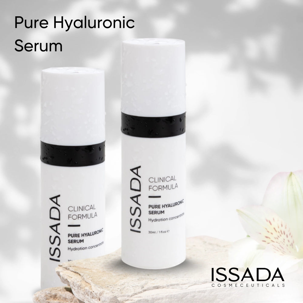 Two bottles of Issada Pure Hyaluronic Serum displayed on natural stone with soft floral accents, showcasing the minimalist and hydrating essence of the skincare product.