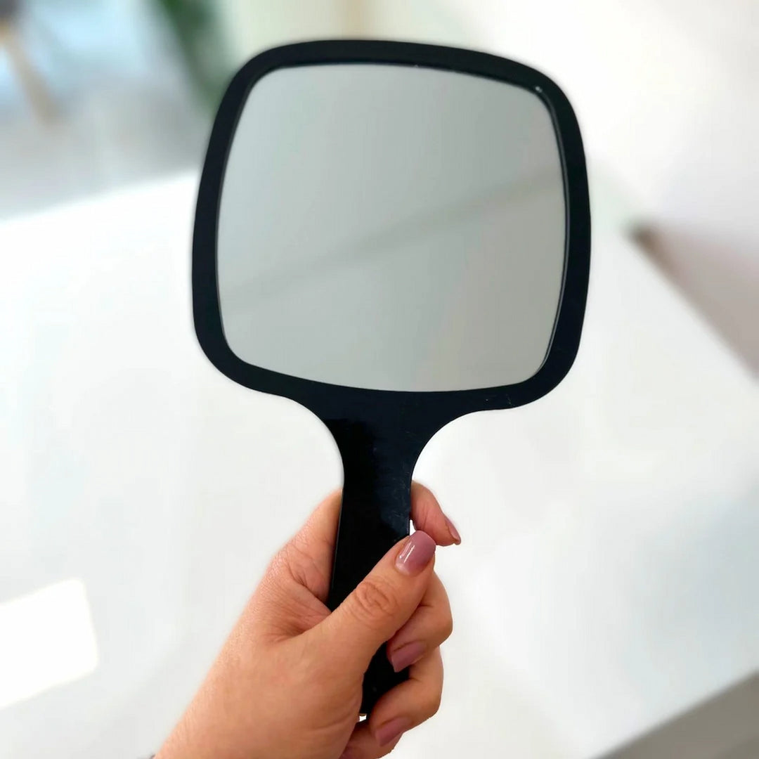 Person holding a sleek black Issada makeup hand mirror for beauty and skincare use.