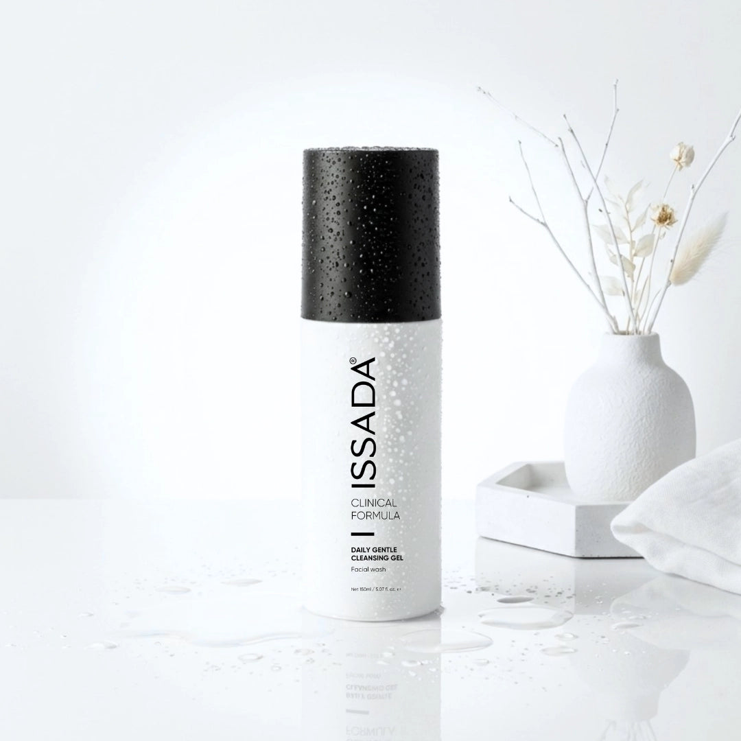 ISSADA Daily Gentle Cleansing Gel bottle with water droplets on a white surface beside a vase with dried stems.