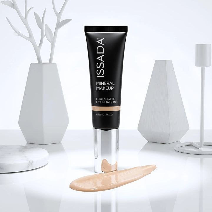 ISSADA Elixir Liquid Foundation tube displayed upright with a beige foundation swatch on a glossy white surface.
