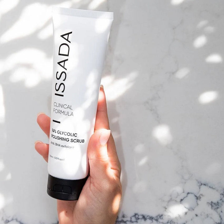 Hand holding ISSADA 14% Glycolic Polishing Scrub exfoliant against marble background