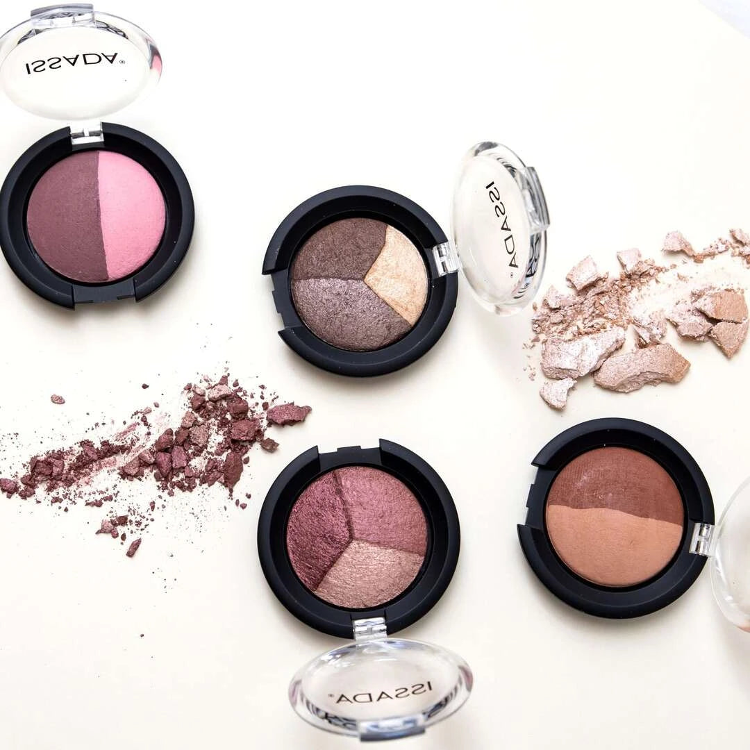 Flatlay of ISSADA Mineral Baked Eye Shadows in duo and trio compacts with crushed pigment swatches on a white background