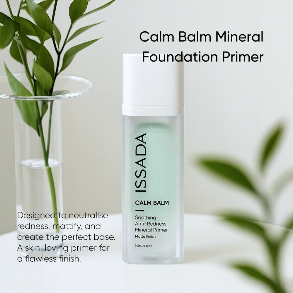 Issada Calm Balm Mineral Foundation Primer displayed on a white table with green leaves in the background, featuring text about its redness-neutralising and mattifying benefits