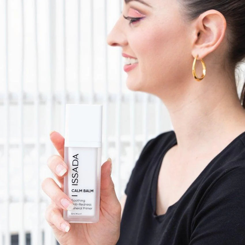 Smiling woman holding ISSADA Calm Balm Anti-Redness Mineral Primer, soothing skincare makeup base for sensitive skin
