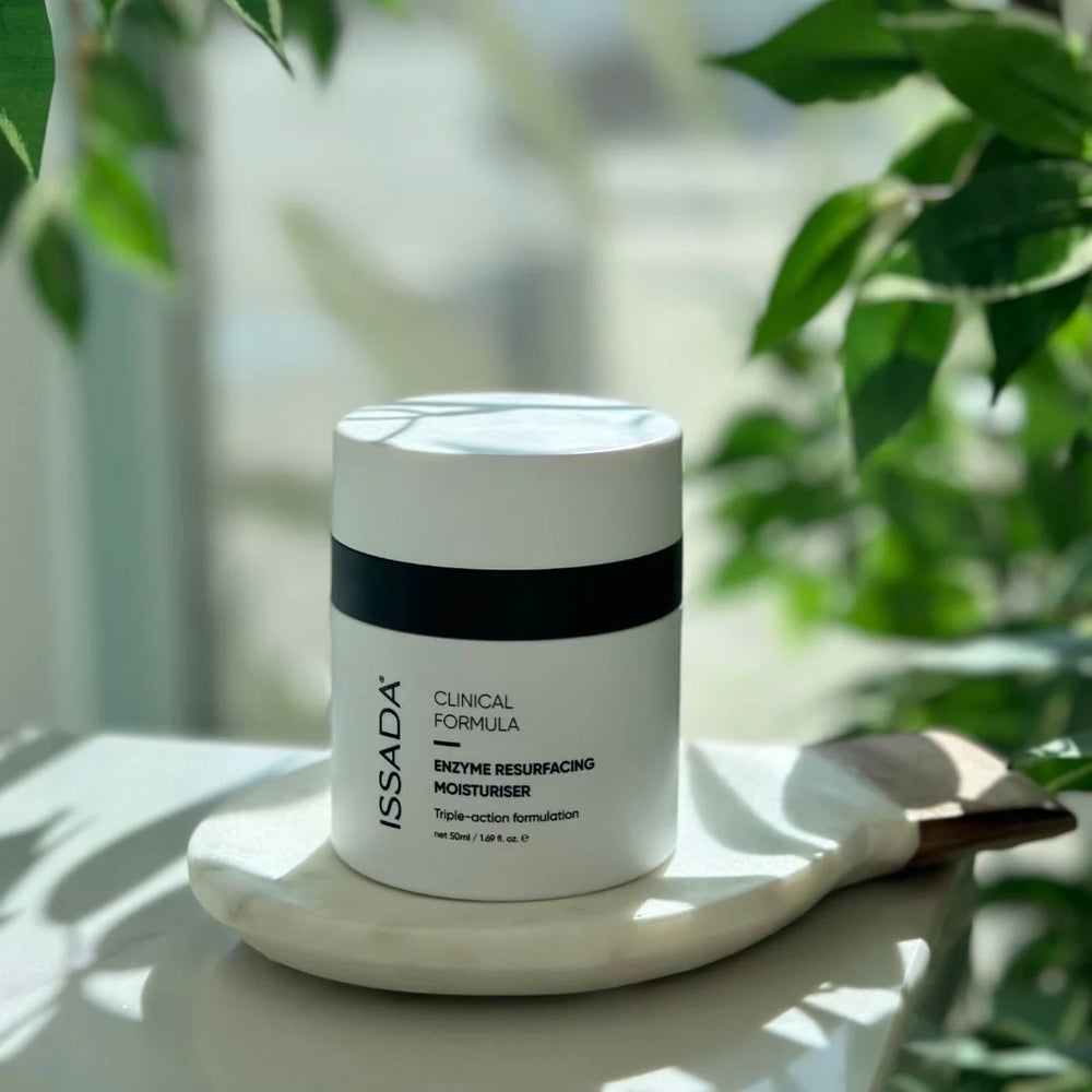 ISSADA Enzyme Resurfacing Moisturiser jar placed on a tray with natural light and green leaves in the background