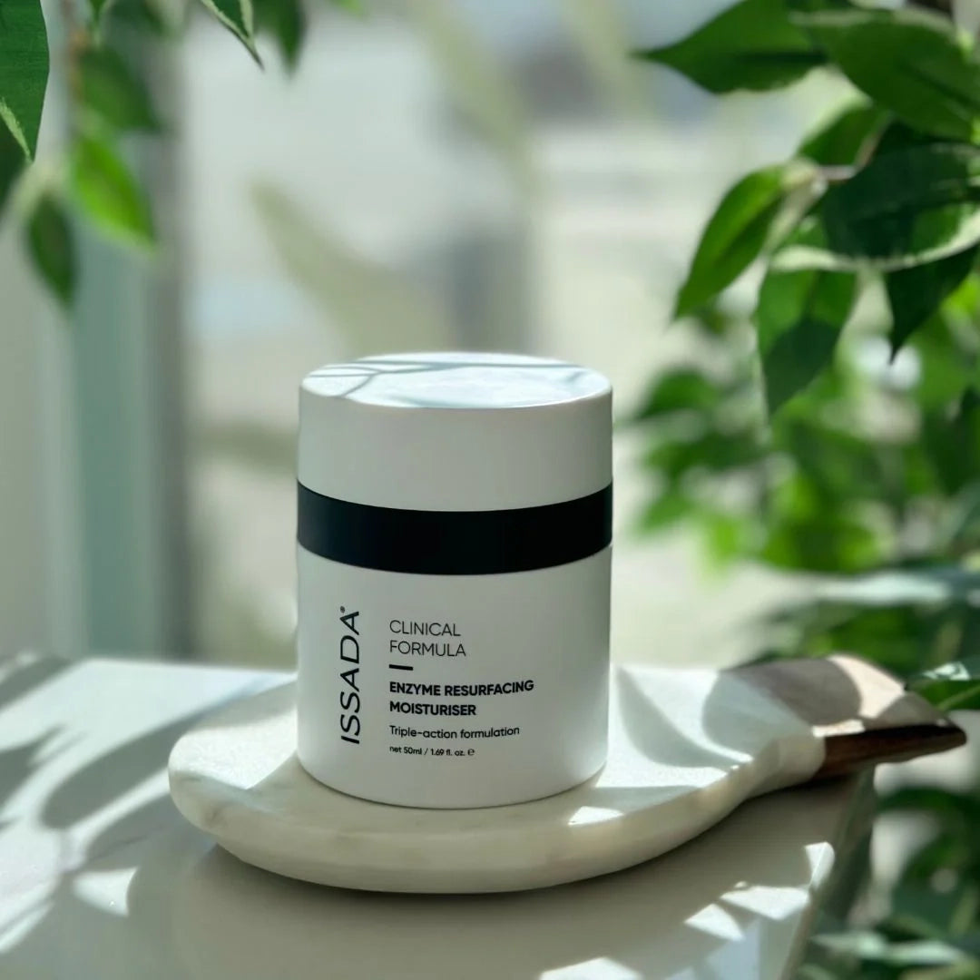 ISSADA Enzyme Resurfacing Moisturiser jar placed on a tray with natural light and green leaves in the background