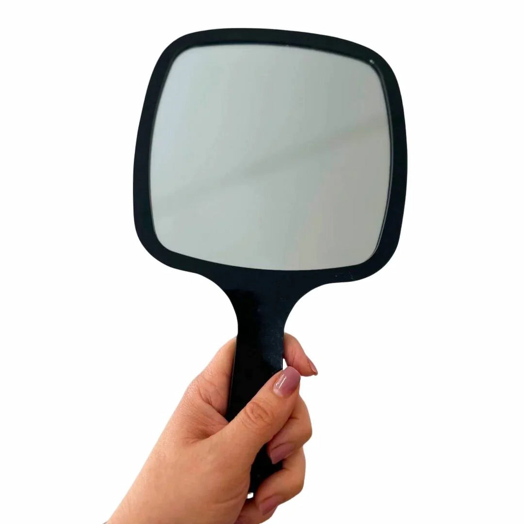 Hand holding Issada black handheld mirror with square design for makeup and skincare use.