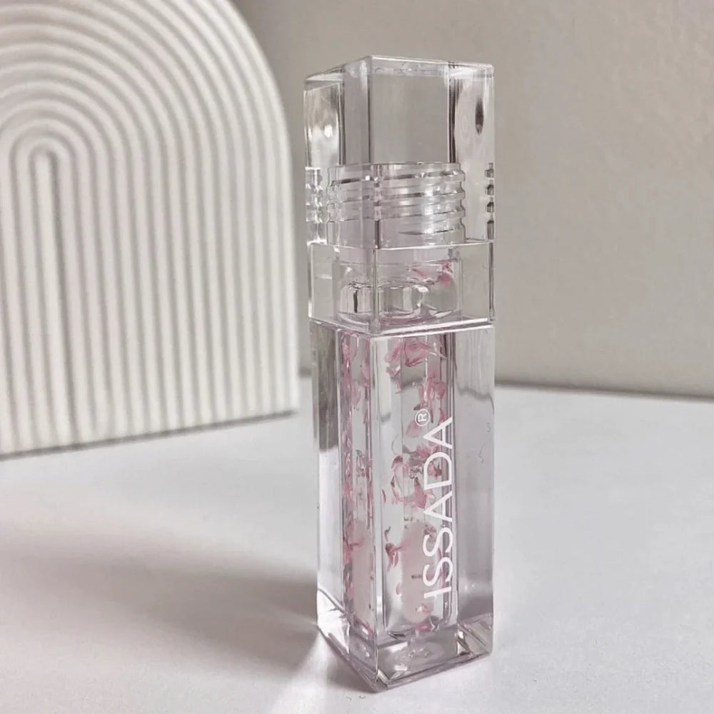 ISSADA Blossom Lip Oil placed on a minimal background, showcasing its hydrating clear formula with real flower petals inside the sleek packaging.