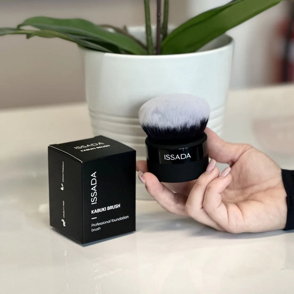 Hand holding Issada Kabuki Brush beside its packaging box, showcasing vegan professional foundation brush with soft dense bristles.