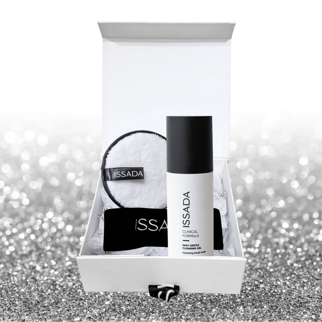 Issada Love Your Skin gift set with Daily Gentle Cleansing Gel, reusable cleansing pad, and makeup headband in a white gift box on a glitter background.