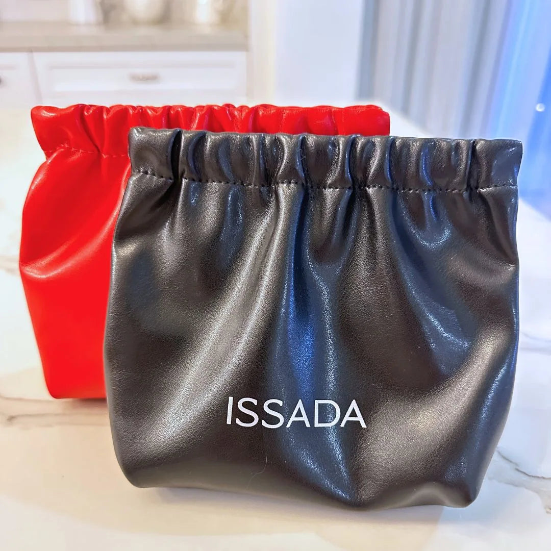 Black and red Issada drawstring makeup pouches placed on a marble surface with the Issada logo on the front.