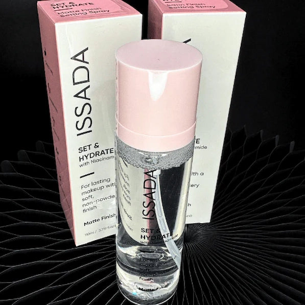 ISSADA Set and Hydrate setting spray, featuring a pink cap and white body, against a black background.