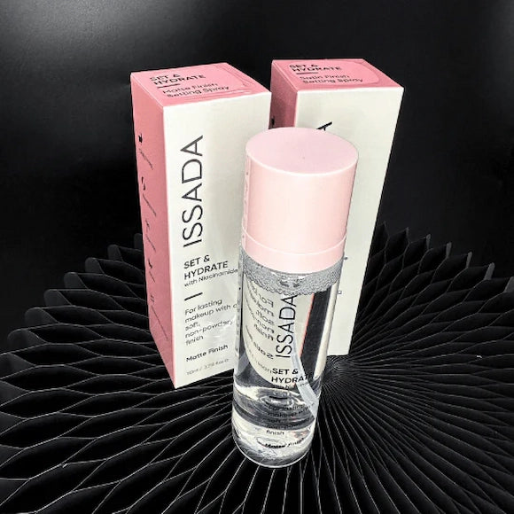 ISSADA Set & Hydrate matte finish setting spray with niacinamide and product with packaging on a black textured surface.