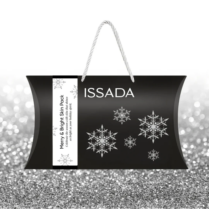 Issada Merry & Bright Skin Pack black festive gift bag with silver snowflakes and white rope handles, displayed on a silver glitter background.