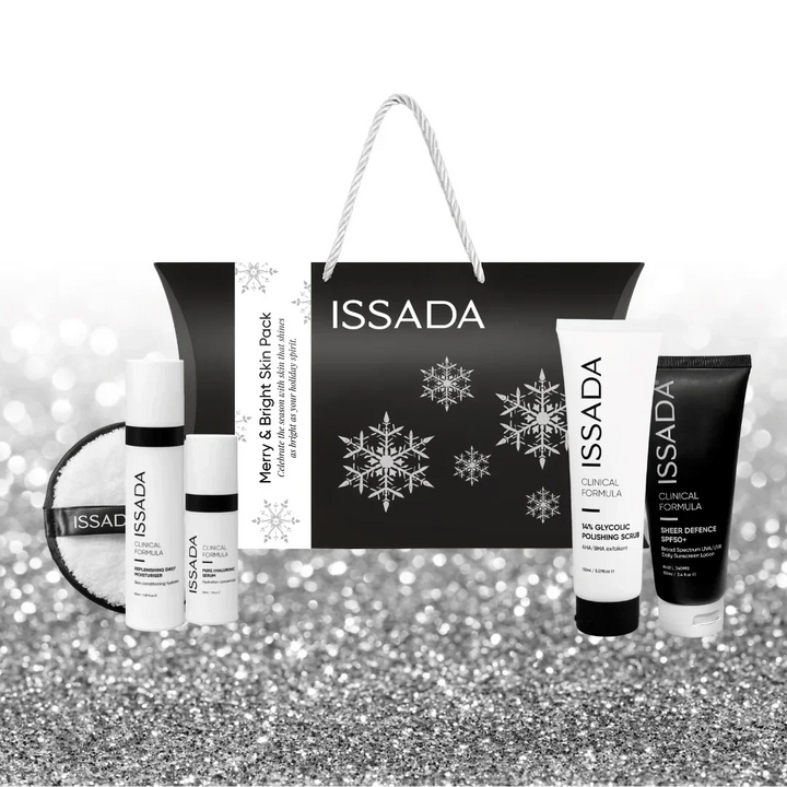 Front view of Issada Merry & Bright Skin Pack, featuring black festive gift bag with silver snowflakes and rope handles, displayed with Clinical Formula skincare products on a silver glitter background.