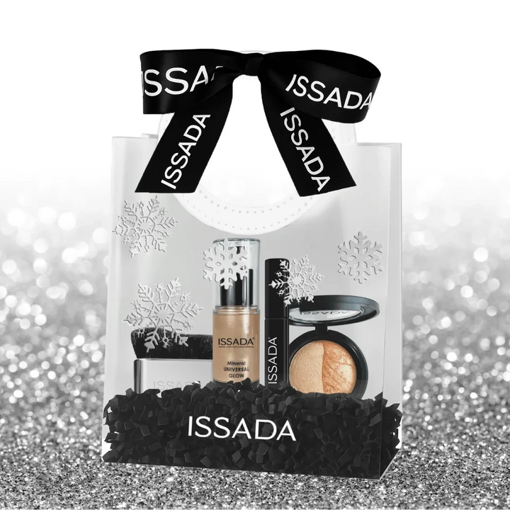 Clear Issada gift bag with black ribbon, snowflake design, and luxury makeup set including glow serum, mascara, brush, and baked highlighter.