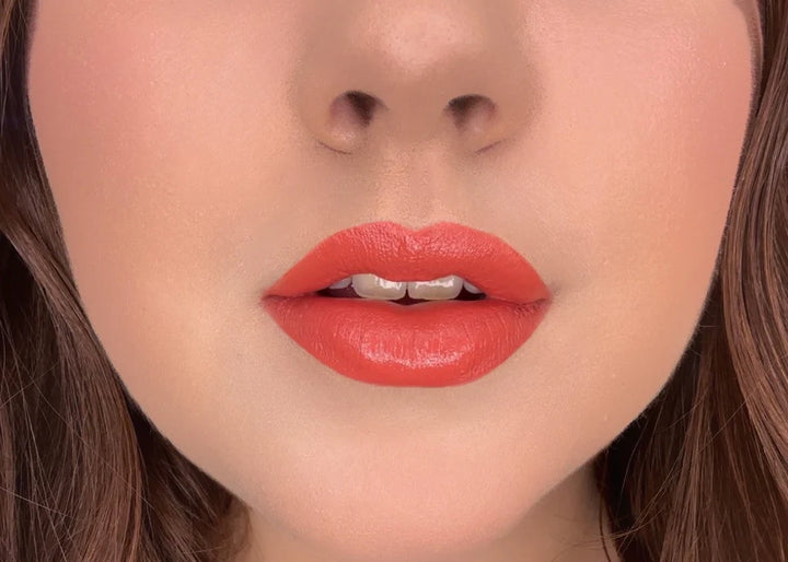 Model wearing ISSADA Mineral Lip Crayons in a vibrant orange-red shade with a creamy matte texture.