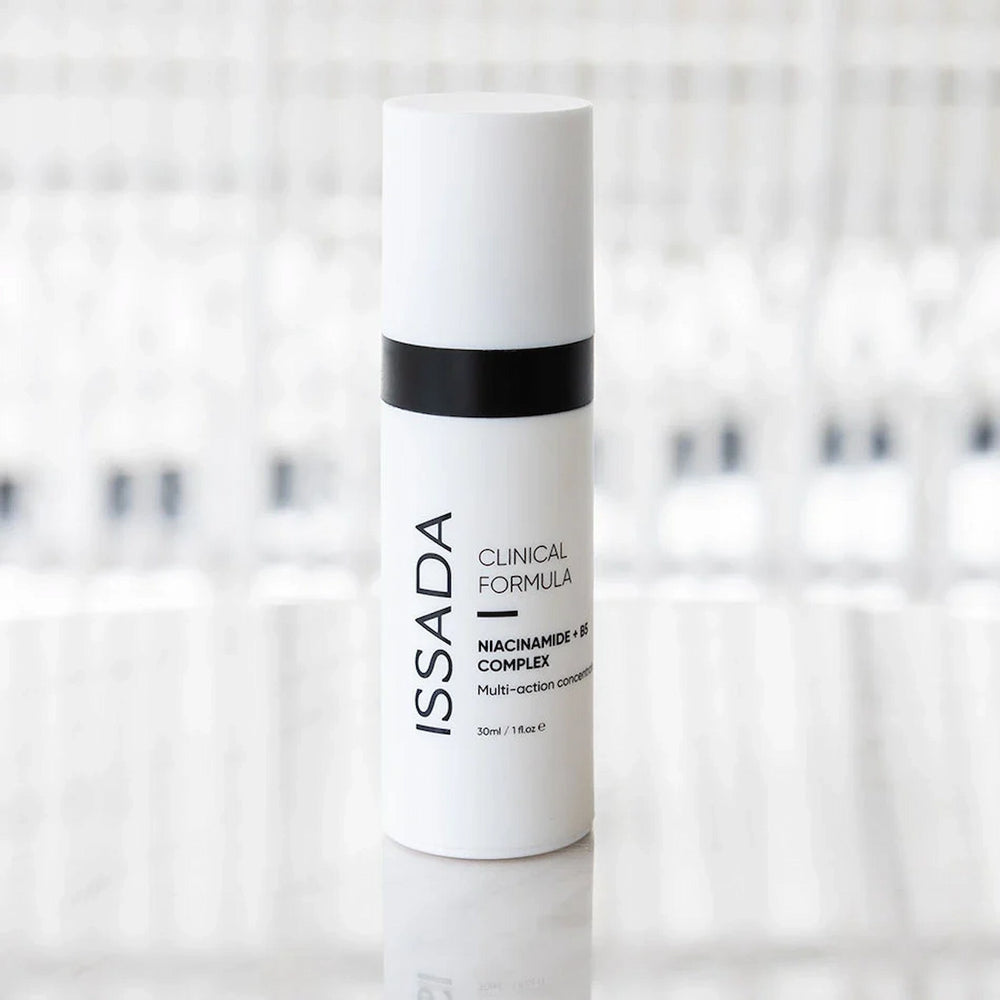 ISSADA Niacinamide + B5 Complex serum bottle on a reflective surface, designed to brighten, hydrate, and strengthen the skin barrier.