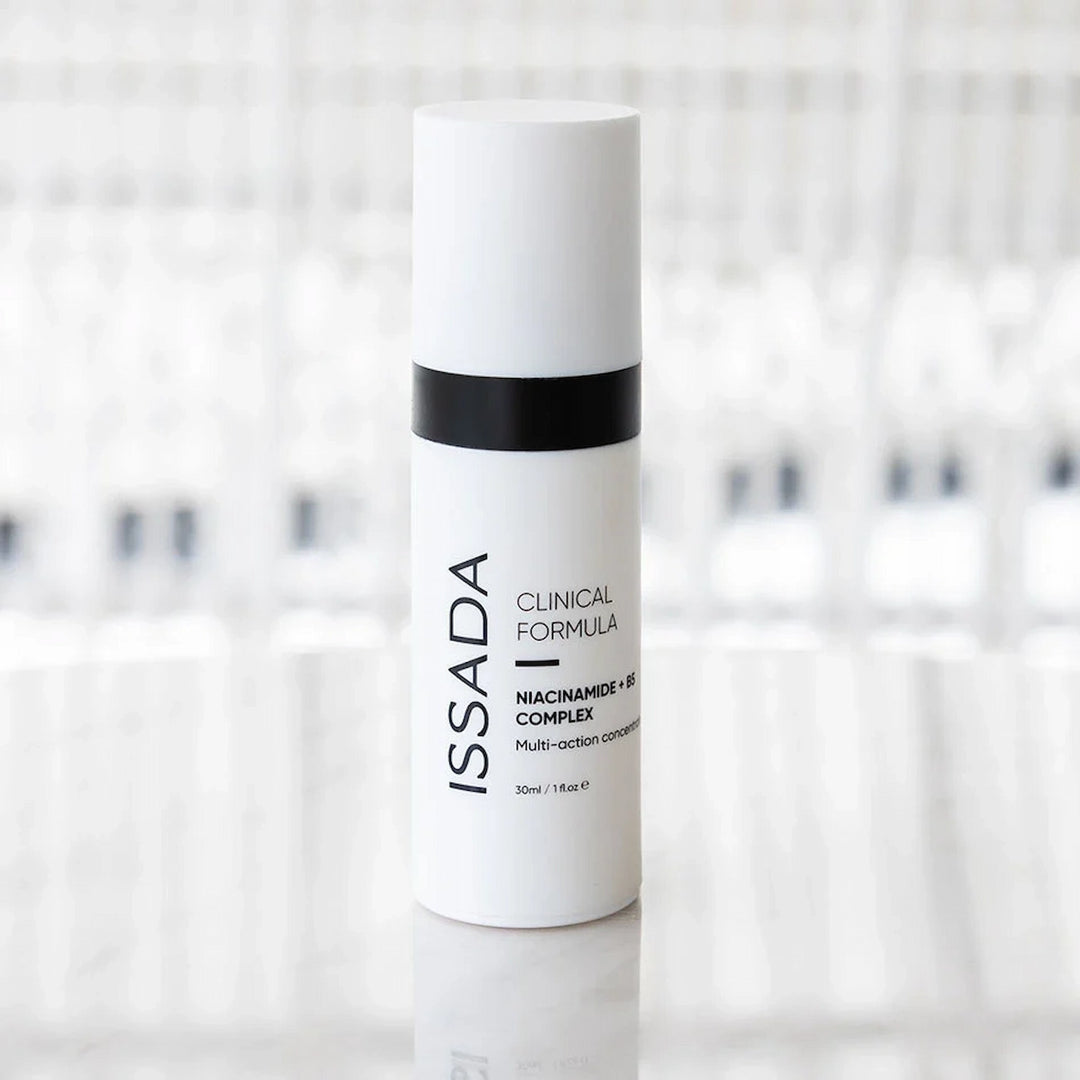ISSADA Niacinamide + B5 Complex serum bottle on a reflective surface, designed to brighten, hydrate, and strengthen the skin barrier.