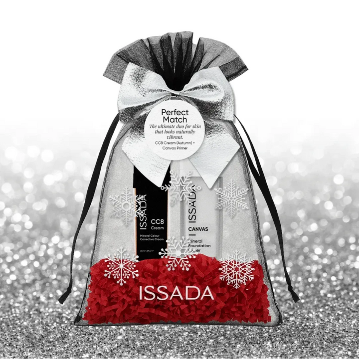 Issada silver and black festive gift bag with snowflake design, featuring CC8 Cream and Canvas Primer with red shredded paper on a glitter background.