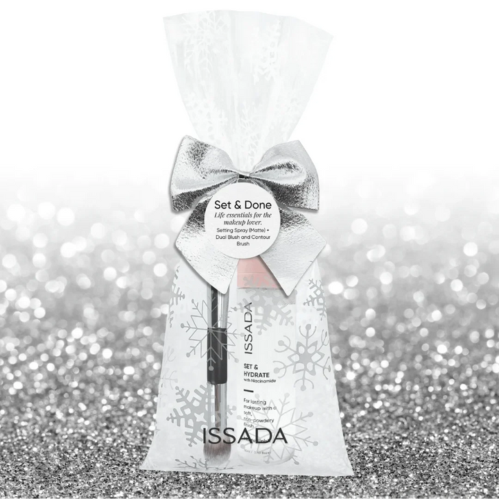 Issada Set & Done gift pack featuring a matte setting spray and dual blush contour brush in a frosted snowflake bag with silver bow on a glitter background.