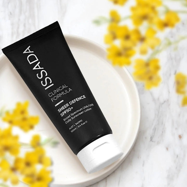 ISSADA Sheer Defence SPF50+ daily sunscreen tube on a white plate with yellow flowers in the background.