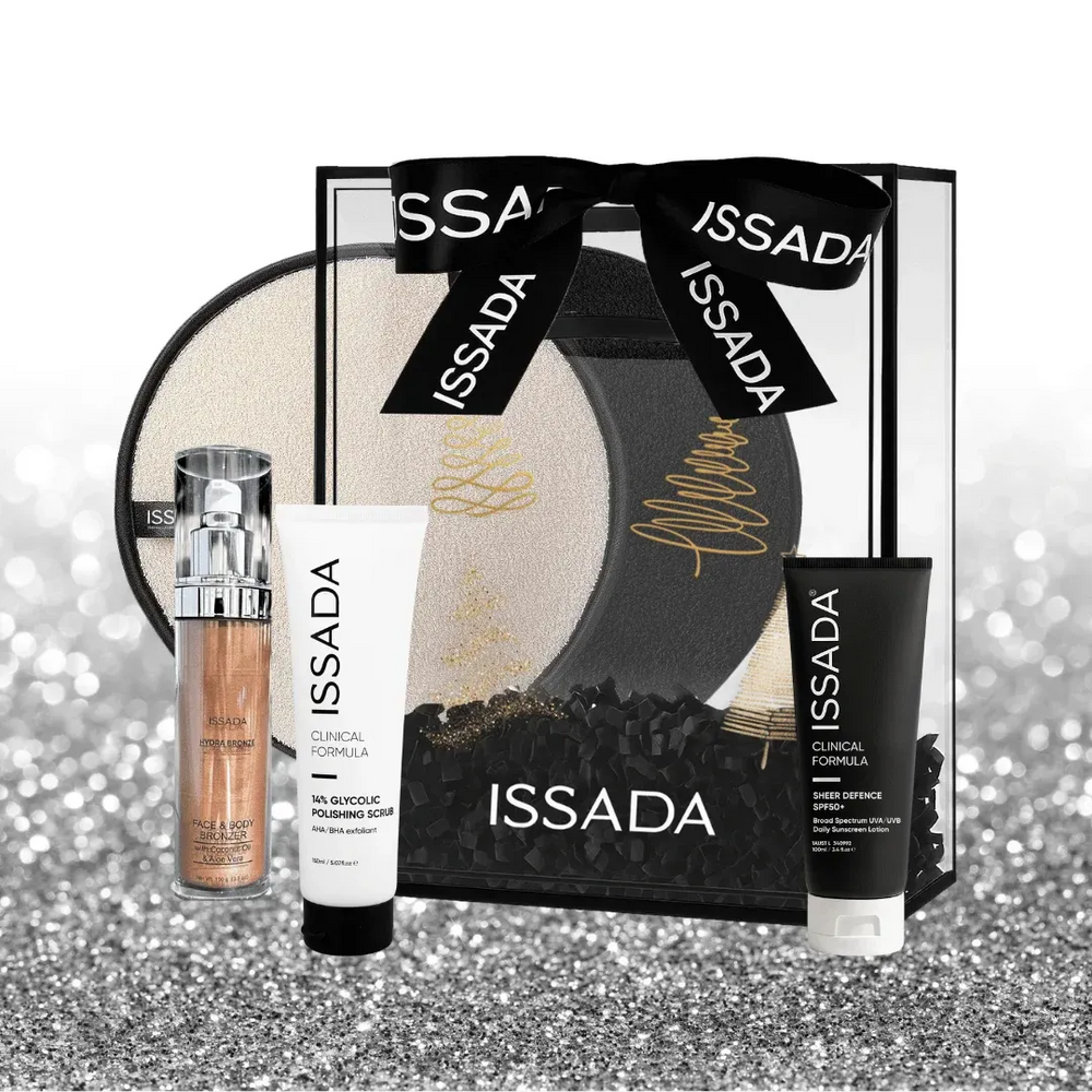 Issada Shimmer Into Summer collection with Hydraglow serum, glycolic polishing scrub, sheer defence SPF50, and cleansing pad displayed outside a clear gift box with black ribbon on a glitter background.