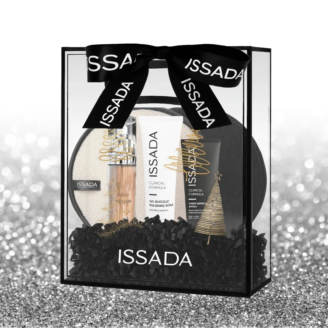 Issada Shimmer Into Summer gift set featuring Hydraglow serum, glycolic polishing scrub, sheer defence SPF50, and cleansing pad in a clear gift box with black ribbon and festive accents on a glitter background.