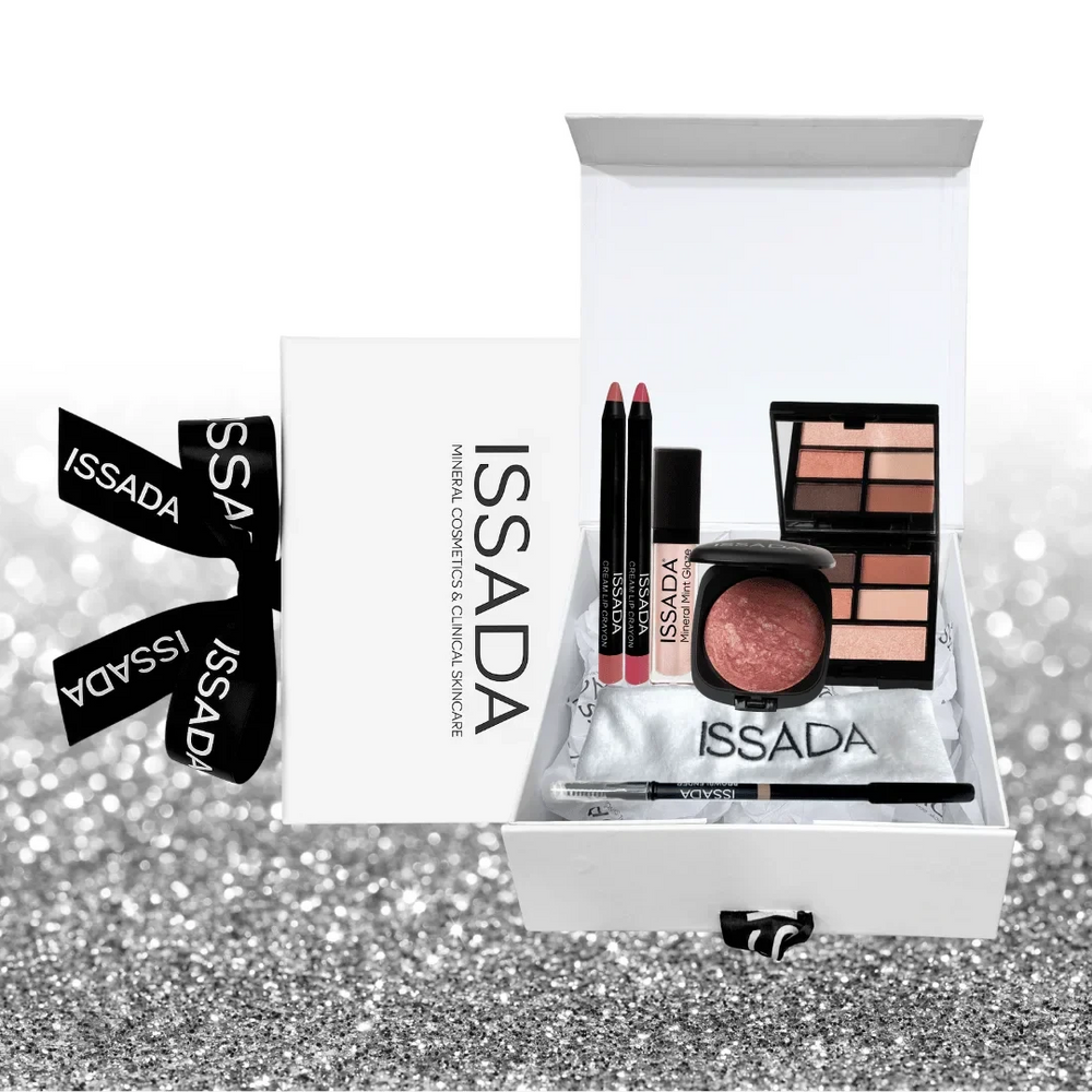 Issada The Party Edit gift box displayed open with lip crayons, baked blush, mineral gloss, eyeshadow palette, and eyeliner on a silver glitter background.