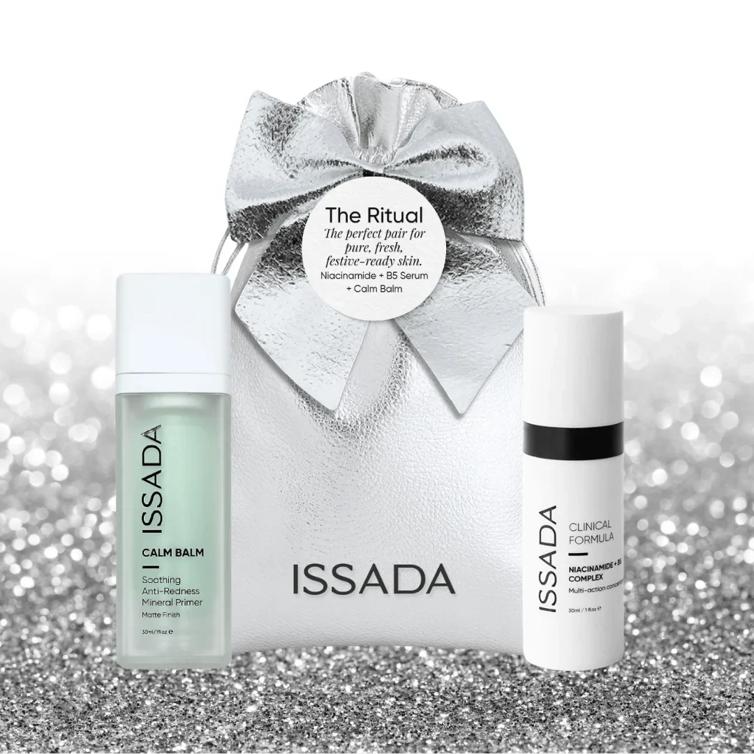 Issada silver holiday gift bag with bow, featuring Calm Balm soothing mineral primer and Niacinamide B5 Complex serum on a silver glitter background.