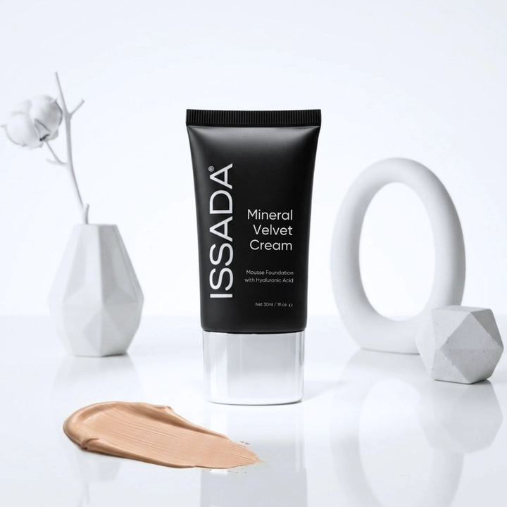 ISSADA Mineral Velvet Cream tube displayed with a beige foundation swatch and white geometric decor on a glossy surface.