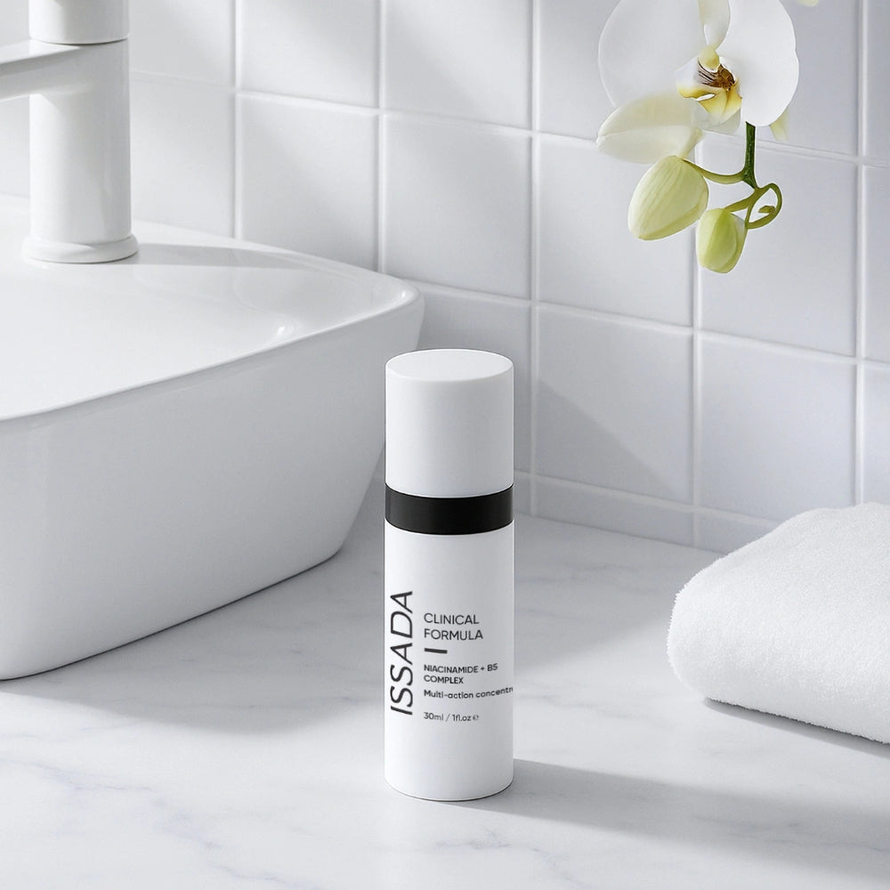 ISSADA Niacinamide + B5 Complex bottle on a bathroom counter beside a white towel and orchid.