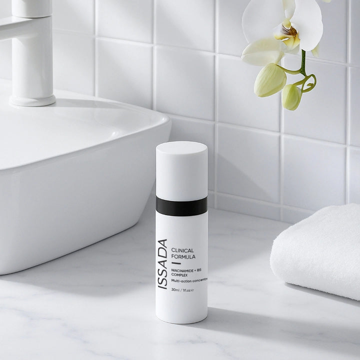 ISSADA Niacinamide + B5 Complex bottle on a bathroom counter beside a white towel and orchid.