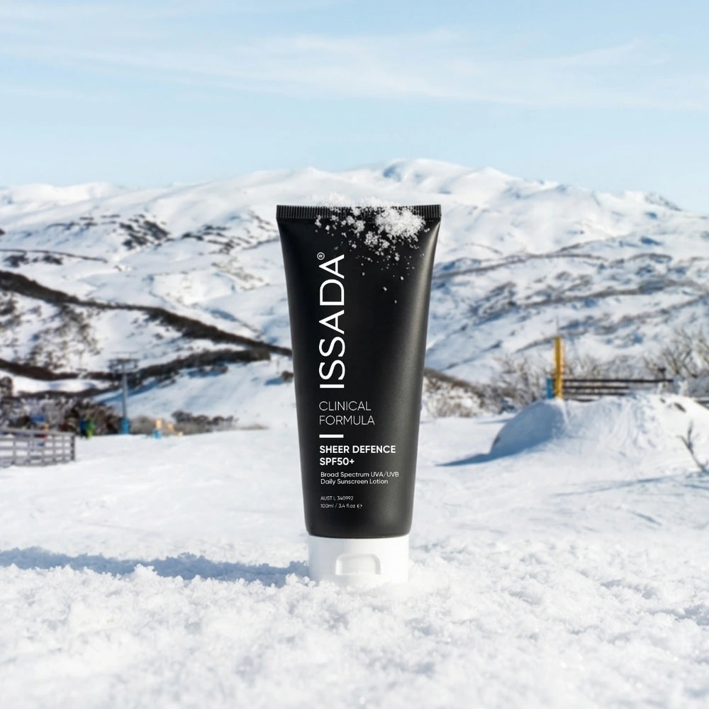 ISSADA Sheer Defence SPF50+ sunscreen tube standing in snow with snowy mountains and blue sky in the background.