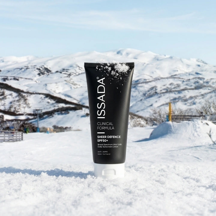 ISSADA Sheer Defence SPF50+ sunscreen tube standing in snow with snowy mountains and blue sky in the background.